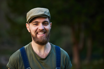Naklejka na ściany i meble Handsome smiling bearded man in green hat in garden
