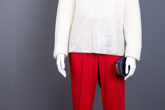 Mannequin in female brand apparel. White knitted sweater and red trousers for women, cropped image. Mannequin with blue leather purse.