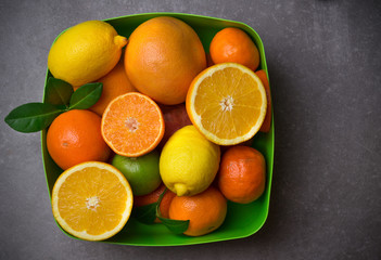 Ripe citrus fruits in green bowl on the dark stone table. flat lay