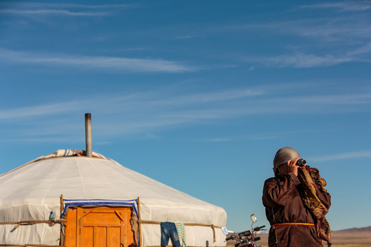 A Mongolian nomad scans the distant horizon with a monocular, looking for members of her family returning to the camp.