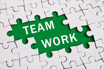 White jigsaw puzzle in assembled state with missing elements forming a green space with white inscription. Team work