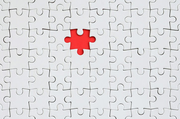 The texture of a white jigsaw puzzle in an assembled state with one missing element forming a red...