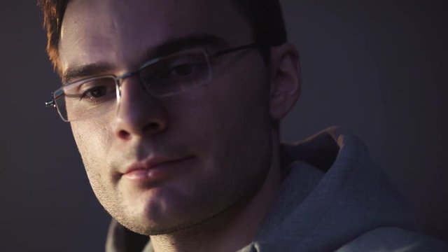 Young unshaved caucasian man in glasses sitting in front of computer at night start smiling recived an achivement, close up portrait