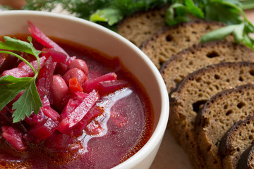 Borscht-vegetable beetroot soup, on the table with slices of rye cereal bread and gluten of sour cream, garlic and herbs. Rustic style.