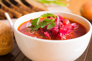 Borscht-vegetable beetroot soup, on the table with slices of rye cereal bread and gluten of sour cream, garlic and herbs. Rustic style.
