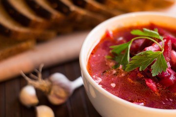 Borscht-vegetable beetroot soup, on the table with slices of rye cereal bread and gluten of sour cream, garlic and herbs. Rustic style.