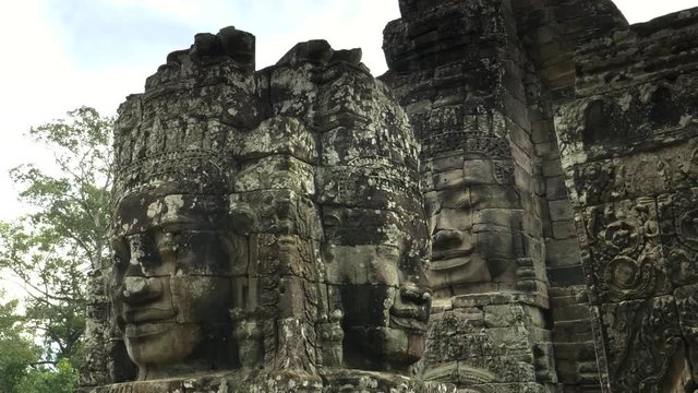 low angle panning shot of carved stone face towers at bayon temple in the angkor wat region of cambodia