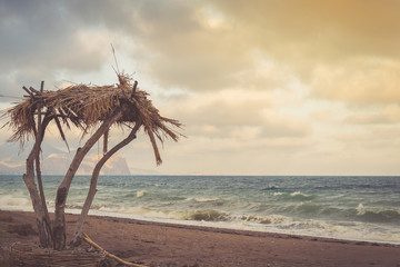 Palm tree, bungalow against the blue stormy sea at sunset