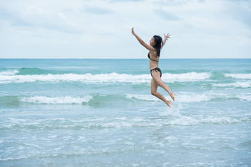 beauty women with brown swimsuit bikini jumping on a beach and wave sea