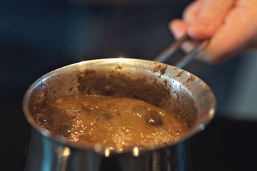 Fototapeta na wymiar Man preparing turkish black coffee on the kitchen stove in a metal pot