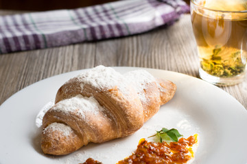 Breakfast with herbal tea and croissant on wooden vintage table