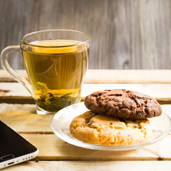 Transparent cup with herbal tea and an American chocolate chip cookie on a transparent plate on a wooden table