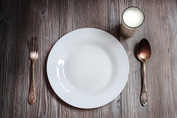 empty white plate and a glass of milk on a dark wooden background.