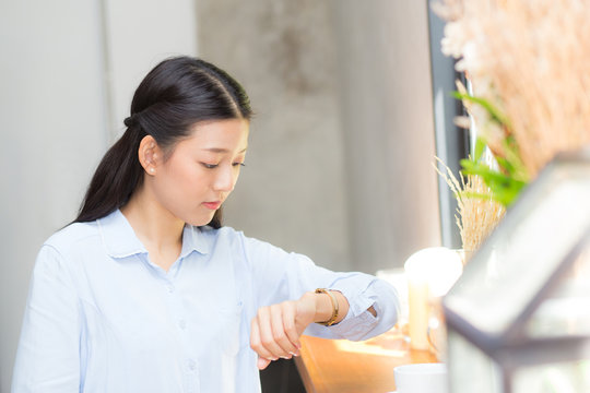 Beautiful asian young woman look at watch waiting for friend or someone, girl checking clock with appointment at coffee shop.
