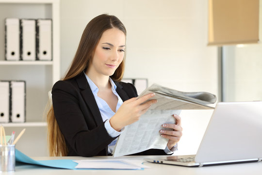 Serious businesswoman reading a newspaper at office