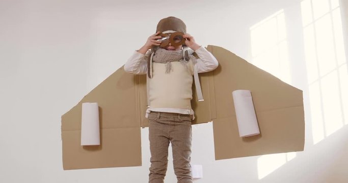 A girl in the bedroom dressed as an airman or a pilot pretends to drive a paper airplane and imagines she is flying free in the sky. Concept of: freedom, success, dreams and play.