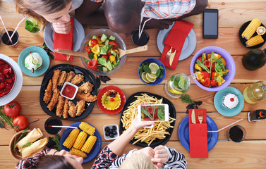 Top view of group of people having dinner together while sitting at wooden table. Food on the table. People eat fast food.