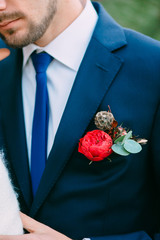 Groom in a blue tuxedo with red rustic boutonniere. Boutonniere on the groom's jacket. Artwork - 191931983