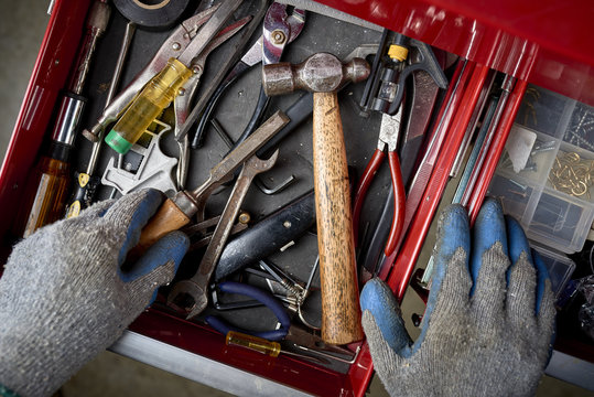 a man opening a tool drawer and holding a chisel inside a workshop.