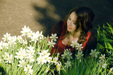 woman in boho style dress sat down to relax near the flowerbed with daffodils in the Park