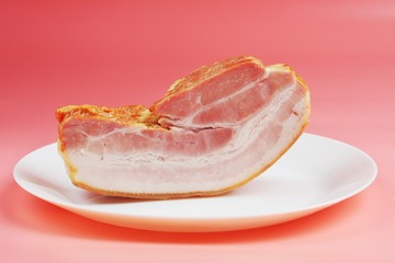 a large fatty piece of smoked bacon lies on plates on a pink background