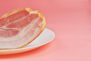 a large fatty piece of smoked bacon lies on plates on a pink background
