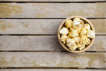 Salted popcorn in round wooden bowl from top view on wooden table background, movie night snack