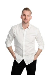 Handsome man standing in front of a white background wearing a white shirt and black jeans looking at camera.