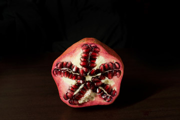 Cut open pomegranate, showing star shape interior - standing up on dark timber background - with...
