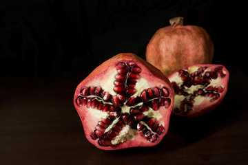Cut open and whole pomegranates on dark timber background - with copy space