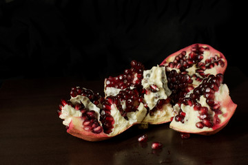 Cut open pomegranate with scattered pomegranate seeds on dark timber background - with copy space