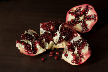 Cut open pomegranate with scattered pomegranate seeds on dark timber background - with copy space