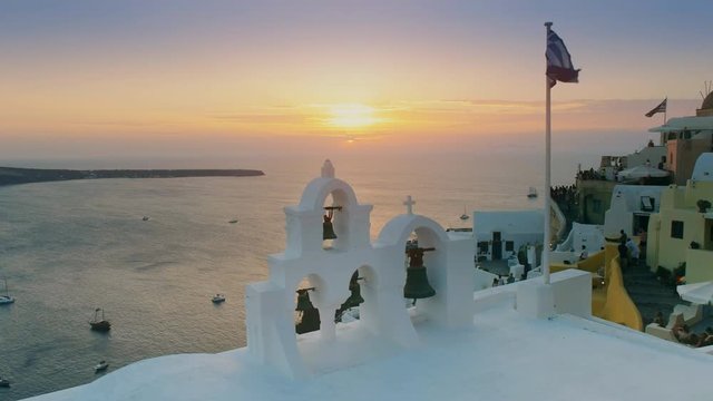 sunset shot of a greek flag and church bells at oia on the island of santorini, greece