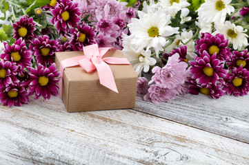 Gift box with mixed flowers in background on white weathered wooden boards
