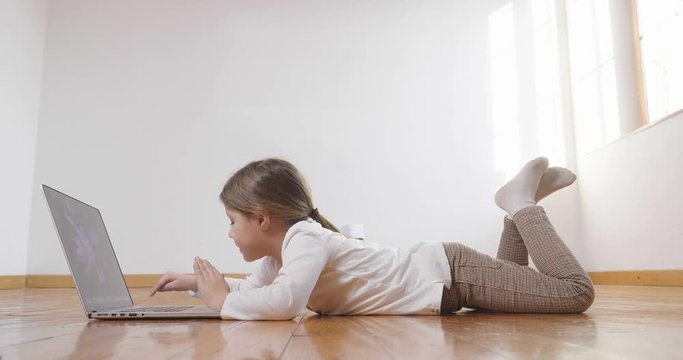 A little girl lying on the floor uses the computer and looks into the camera and smiles. Concept of: computer safety for children, technology, courses for learning