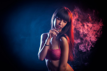 Young dark-haired woman in red lingerie posing against a background of red and red smoke from a wipe on a black isolated background