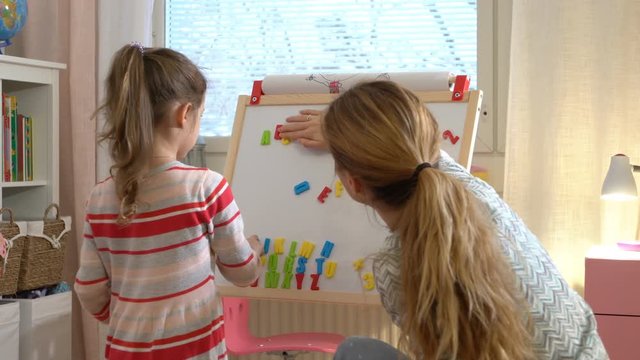 Early childhood development. Little girl are learning to write letters with special desk. Young woman teaching her child the alphabet. Play and learn