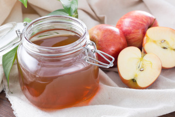 Closeup of glass jar apple juice with fresh apples on table