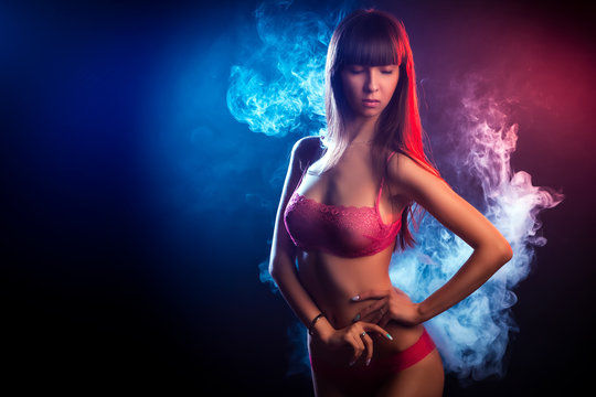 Beautiful woman with dark long hair in red lingerie looks at the camera and posing against a blue and red smoke background from a wipe on a black isolated background