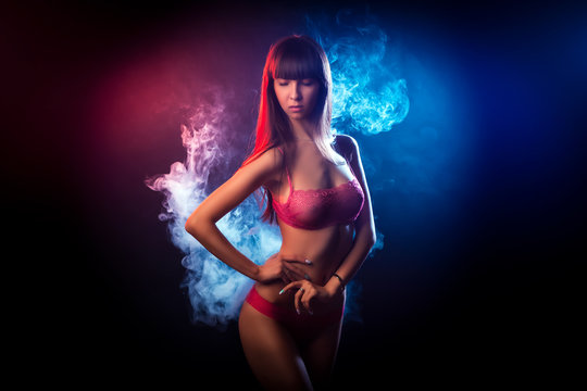 Beautiful woman with dark long hair in red lingerie looks at the camera and posing against a blue and red smoke background from a wipe on a black isolated background