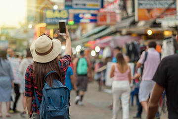 Back side of Young Asian traveling women taking photo in Khaosan Road walking street at night in Bangkok, Thailand, traveler and tourist concept