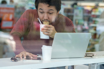 Asian businessman in casual suit eating noodles with urgent action in rush hour at the desk beside the glass in modern office, Business work hard concept