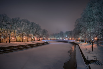 Beautiful view of Aura river with frost covered oak trees on the sides illuminated by streetlight and Turku Cathedral faintly seen in the background in Turku, Finland