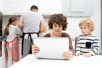 Fototapeta premium Portrait of happy young family enjoying evening at home, focus on mother and son watching videos on laptop in foreground