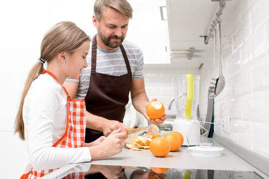 Side View Portrait Of Happy Father Cooking With Daughter Making Orange Juice In Modern Kitchen At Home