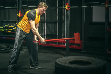 Hard training man strikes a big tyre by a hammer in his hands. Shock power training.