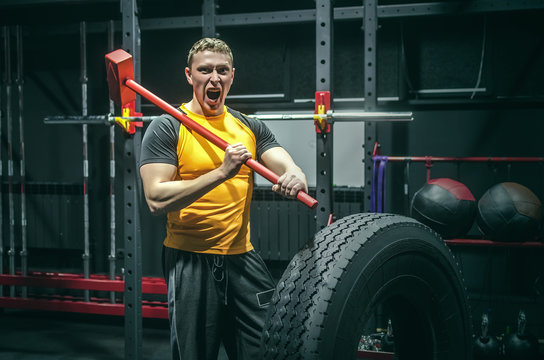Hard training man strikes a big tyre by a hammer in his hands. Shock power training.