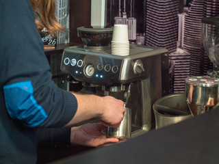 Barista prepares coffee at the coffee machine, close-up. Photo behind the bar counter with blurred background and soft focus.