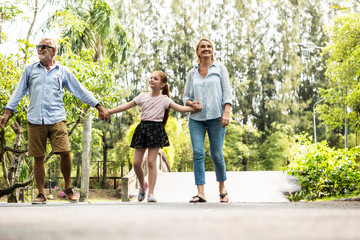 Fototapeta premium Happy family having fun together in the garden. Father, mother and daughter holding hands and walking in a park. Lifestyle concept