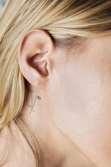 Closeup of a simple behind the ear tattoo of a young woman